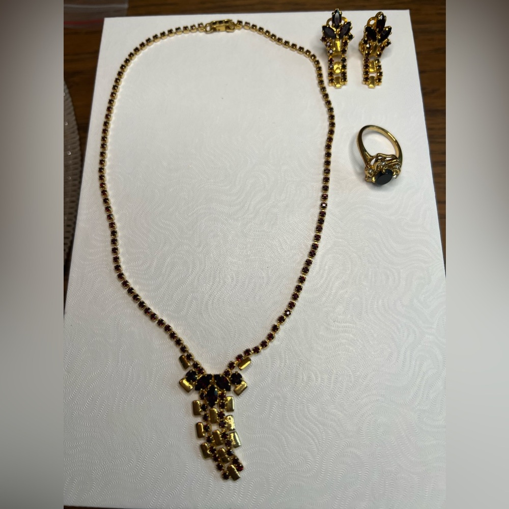 Gold coloured jewelry set with dark red gems; ring is black gems